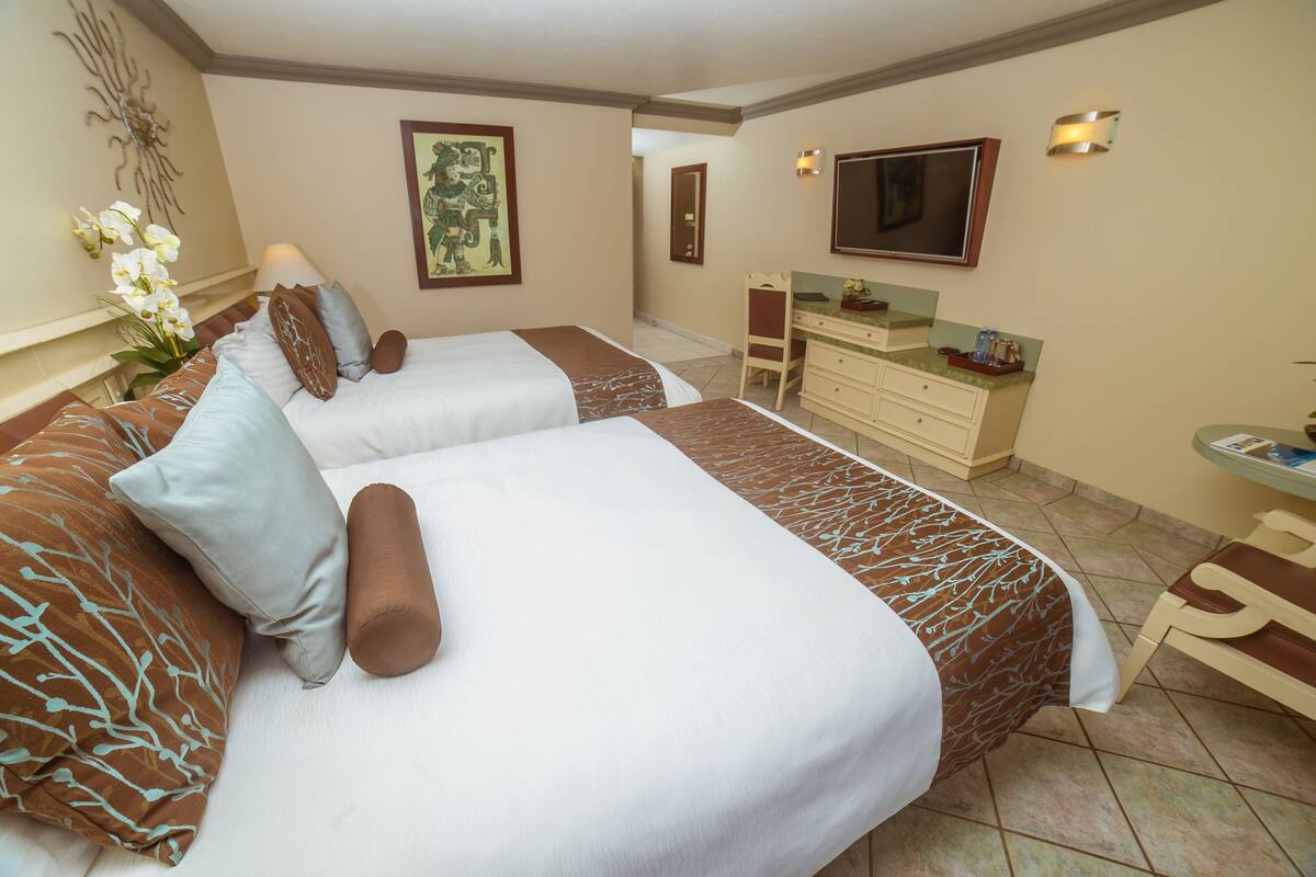 A hotel room with two beds, a desk, a vanity, and a television.
