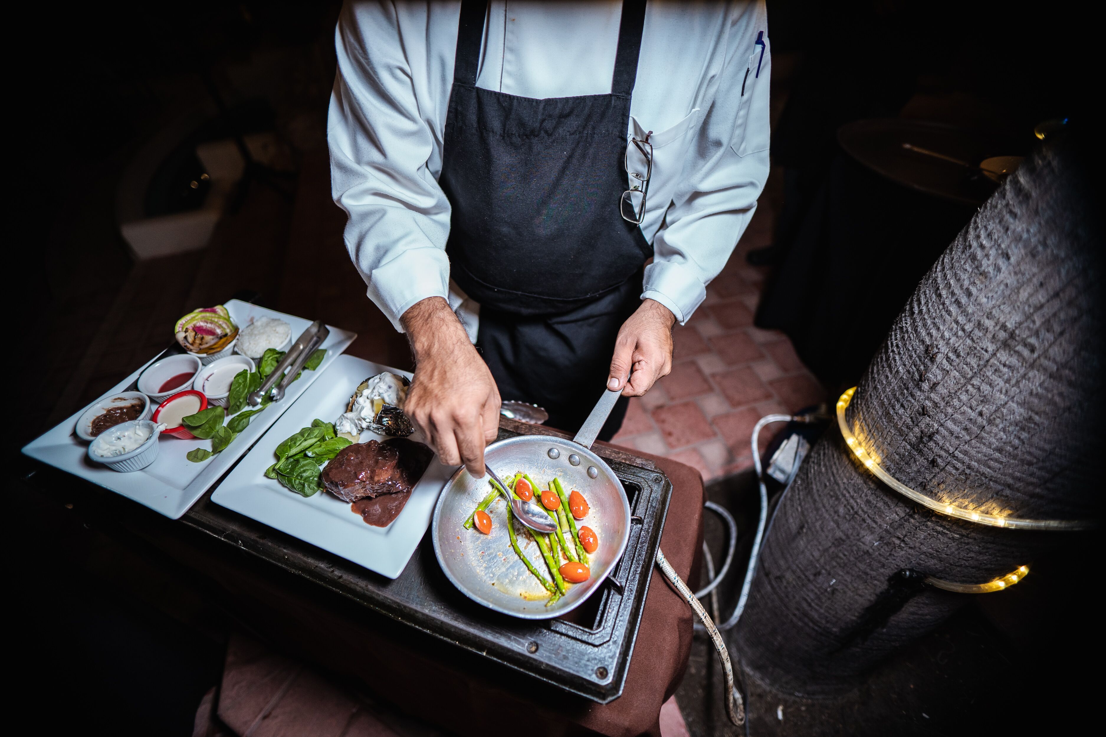 Un chef préparant des aliments sur un gril, avec des assiettes remplies et des ustensiles visibles.