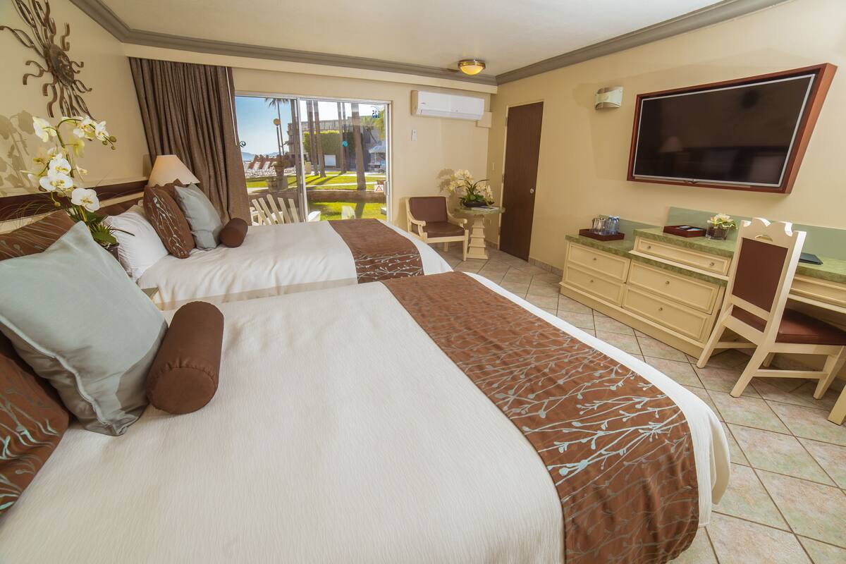 A hotel room with two beds, a desk, a chair, a TV, and a balcony with a view.