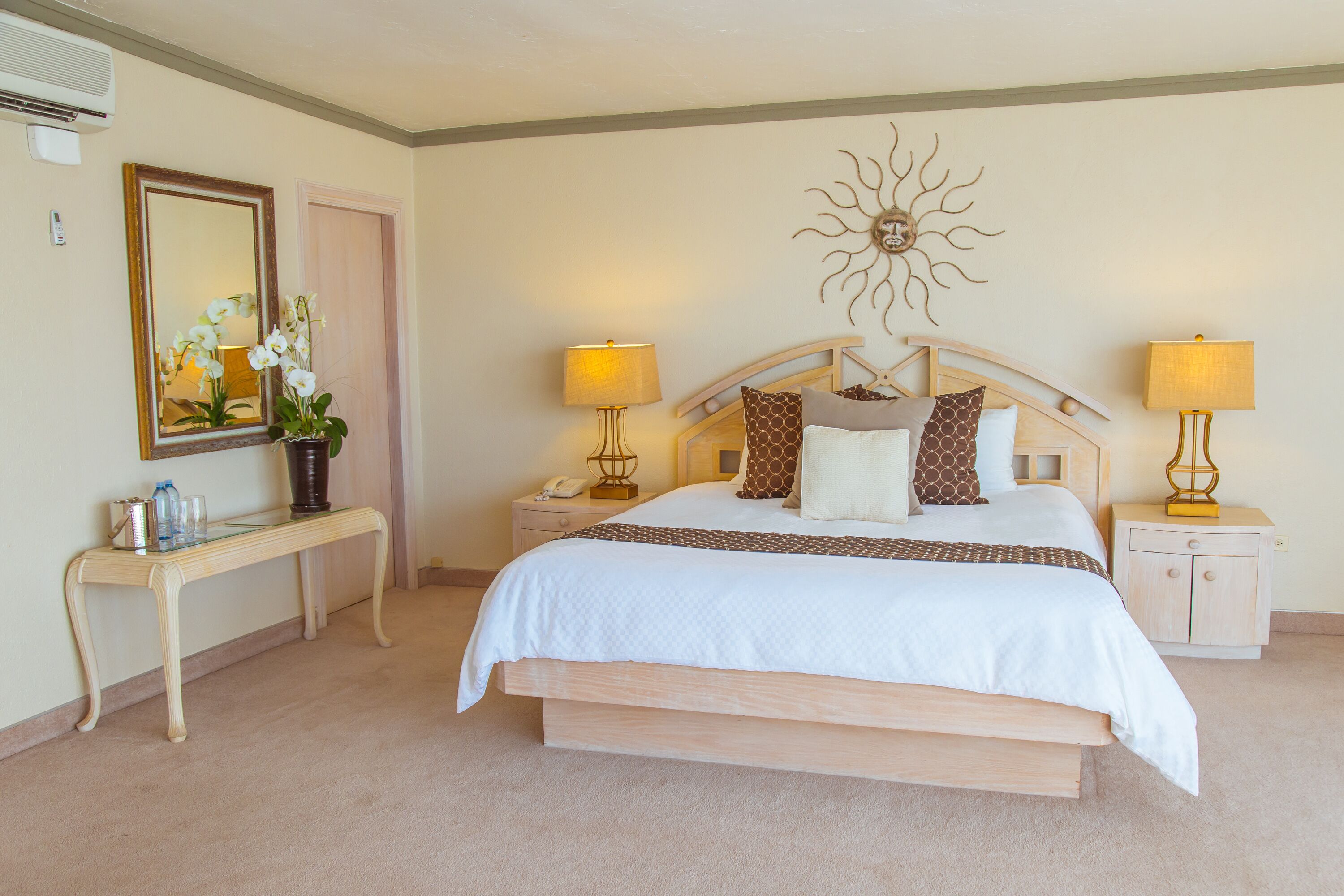 A hotel room with a large bed, bedside tables, a mirror, and a sun-shaped wall decoration.