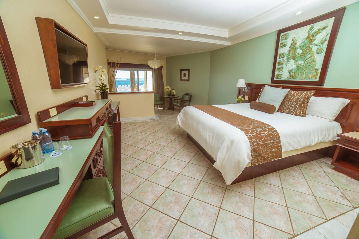 A hotel room with a large bed, a desk with a chair, a television, and a window with a view.