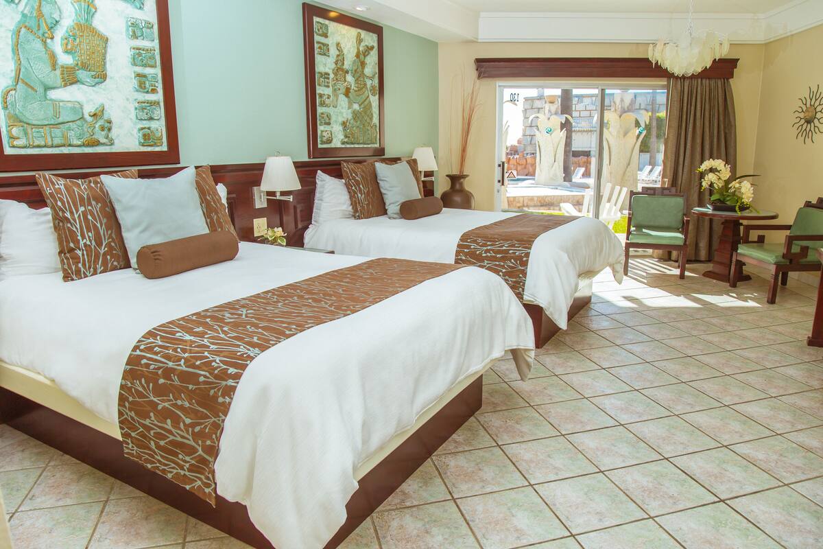 A hotel room with two beds, a dining area, and a view of the outside.