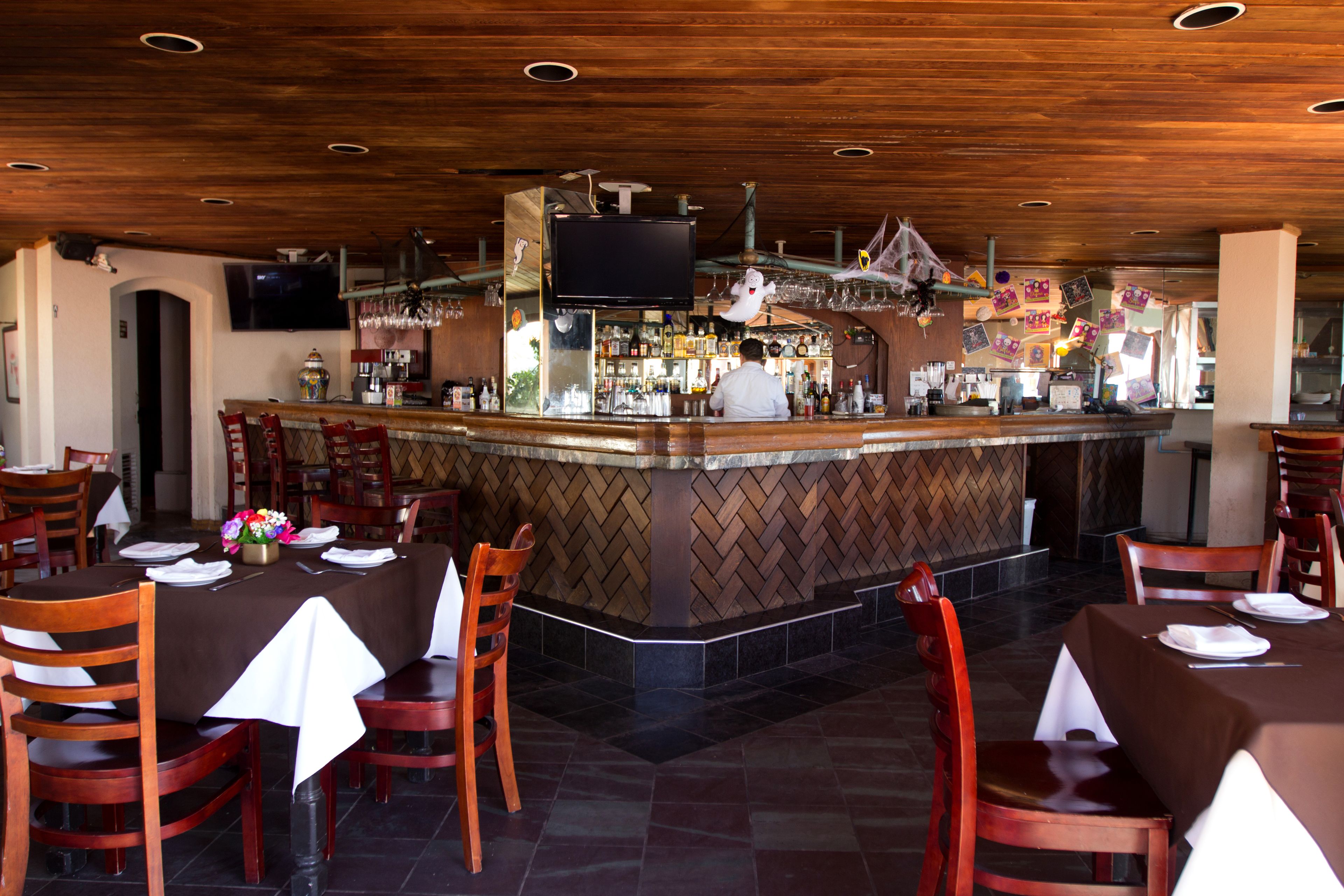 A restaurant with a bar area, wooden ceiling, and tiled floor.