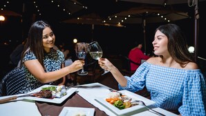 Two people toasting with wine glasses at a table with plates of food. - Estero Beach Hotel & Resort (Ensenada)