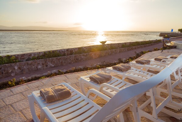 A seaside terrace with white lounge chairs, some with towels, and a small table with a painting. - Estero Beach Hotel & Resort (Ensenada)