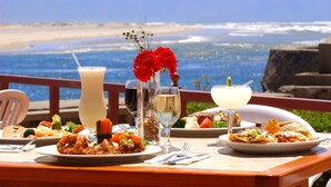 A table set with various dishes and drinks, overlooking a beach and ocean. - Estero Beach Hotel & Resort (Ensenada)
