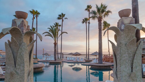 A pool area with stone sculptures, palm trees, and lounge chairs. - Estero Beach Hotel & Resort (Ensenada)