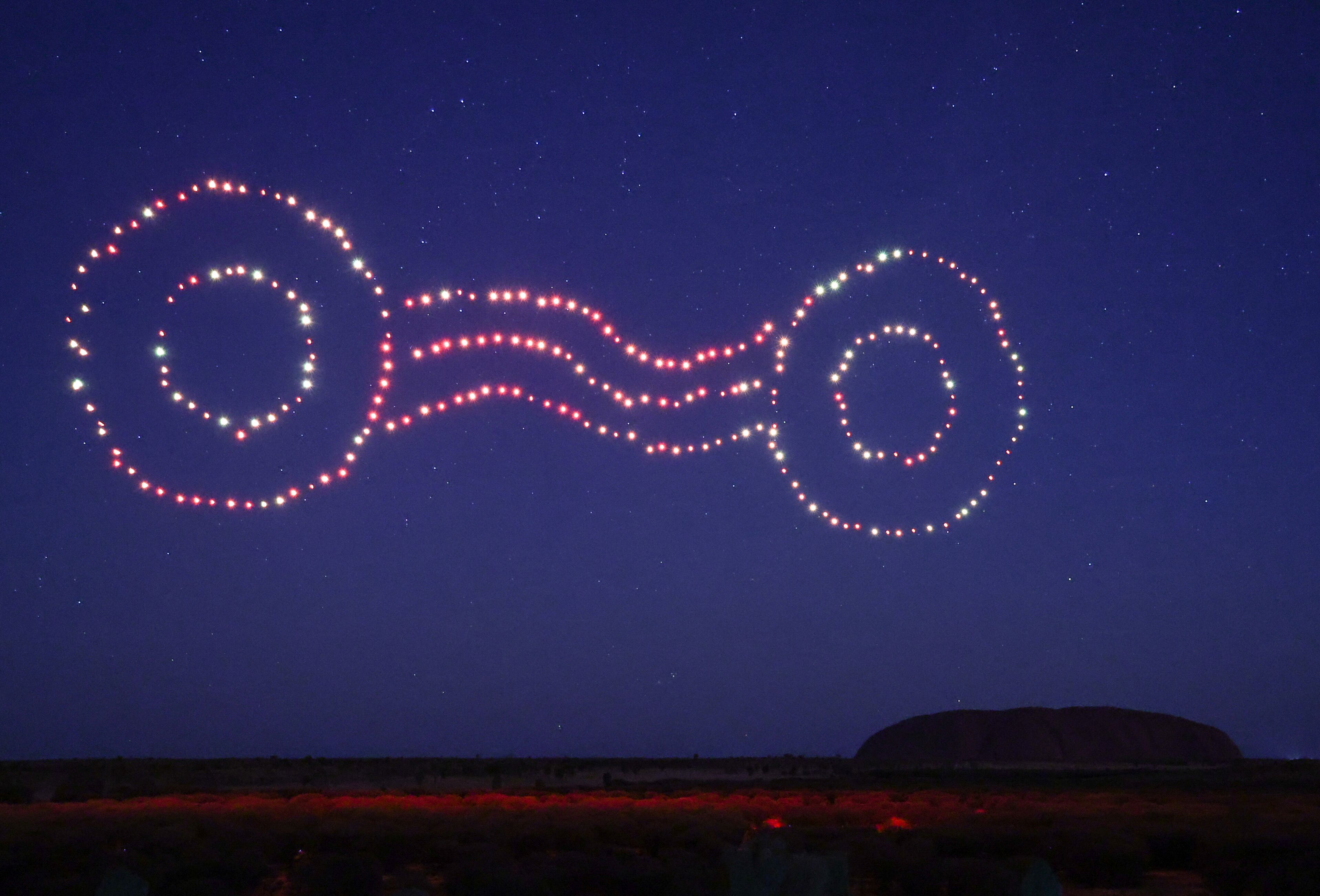 A starry night sky with a large, illuminated structure resembling a figure in the distance.