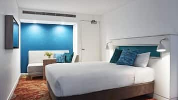 Una habitación de hotel moderna con una cama grande, una mesita de noche, una silla y una pared azul decorativa.