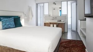 A modern hotel room with a large bed, a bathroom with a sink and mirror, and a TV. - The Lost Camel (Yulara)