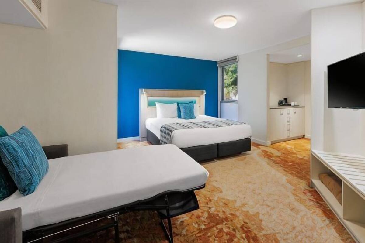 Un dormitorio con cama, sofá, televisión y zona de cocina.