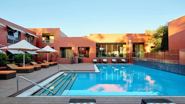 A modern outdoor pool area with lounge chairs, umbrellas, and a clear blue pool. - The Lost Camel (Yulara)