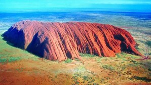 A large red rock formation with a flat top, surrounded by a flat landscape. - The Lost Camel (Yulara)