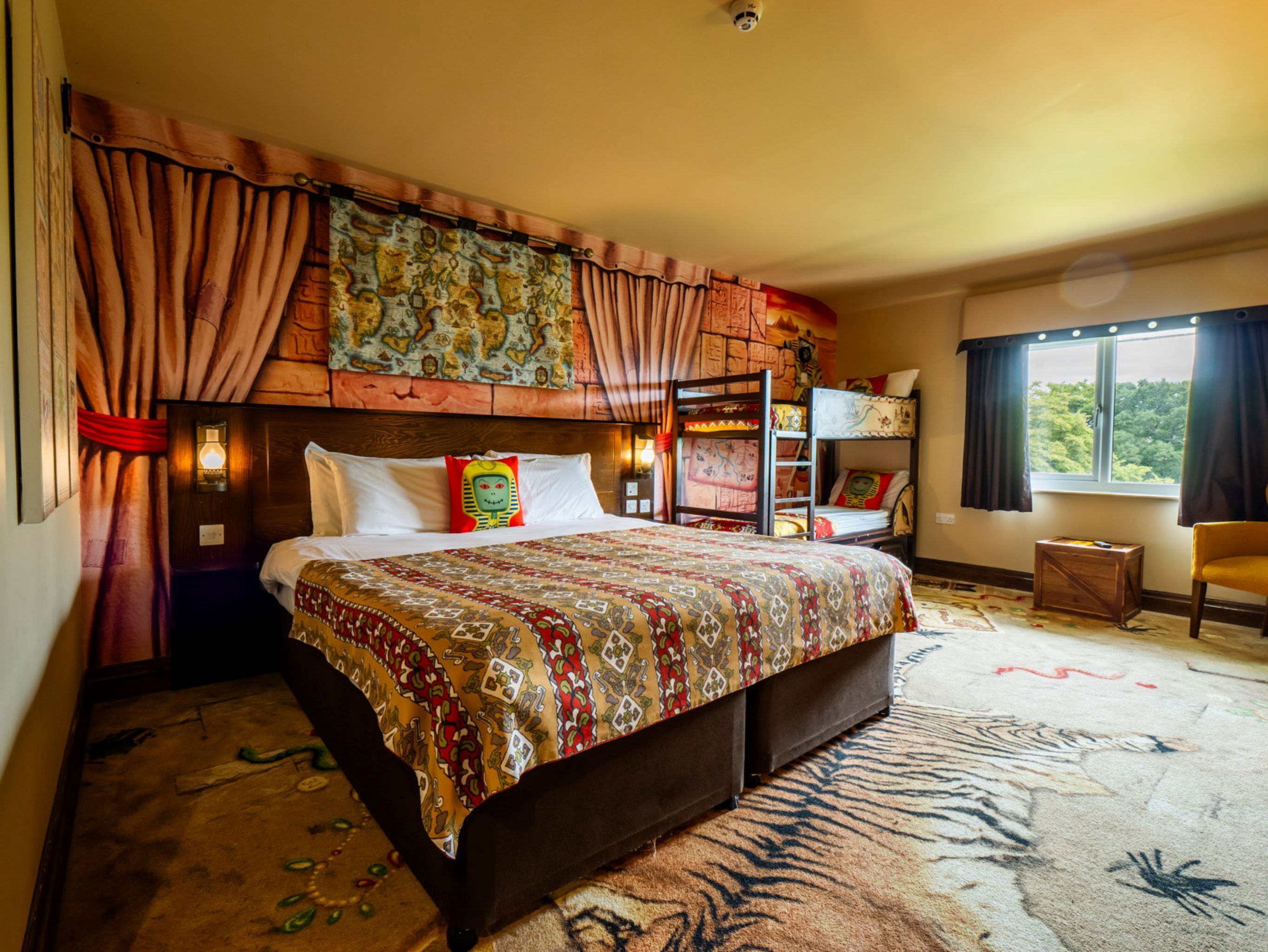 A spacious bedroom with a large bed, a bunk bed, a window with a view, and a small table.