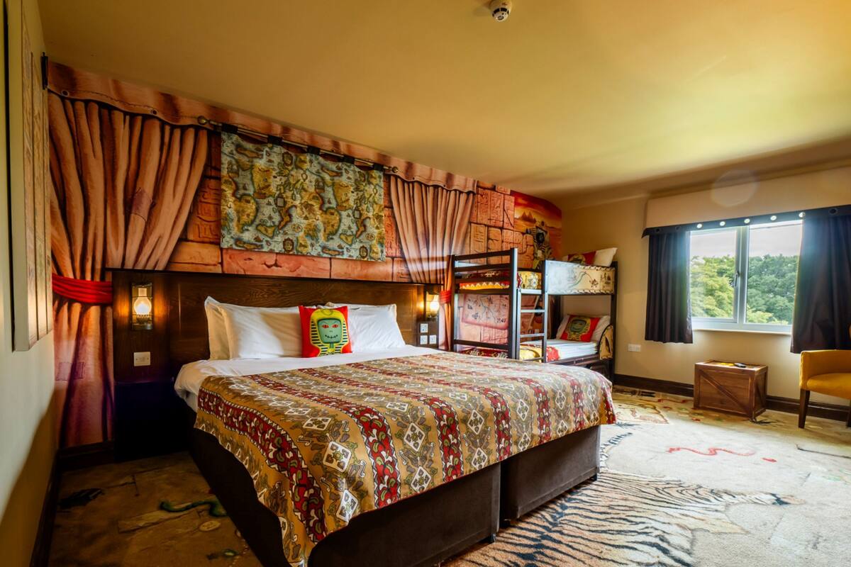 A spacious bedroom with a large bed, a bunk bed, a window with a view, and a small table.