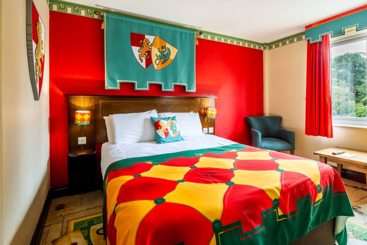 A hotel room with a bed, a chair, a nightstand, and a window with curtains.