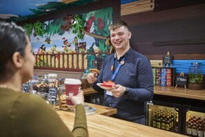 A bar area with a wooden counter, a menu board, and a decorative mural in the background. - Legoland Windsor Resort Hotel (Windsor)