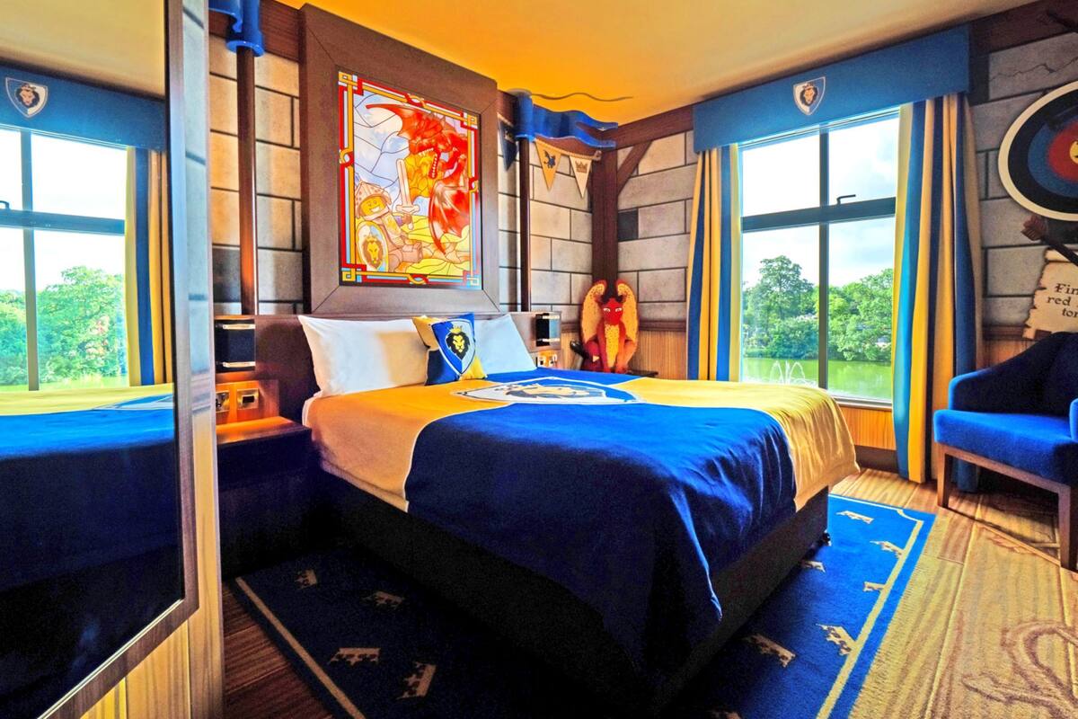 A hotel room with a large bed, a nightstand, a window with a view, and a decorative wall piece.