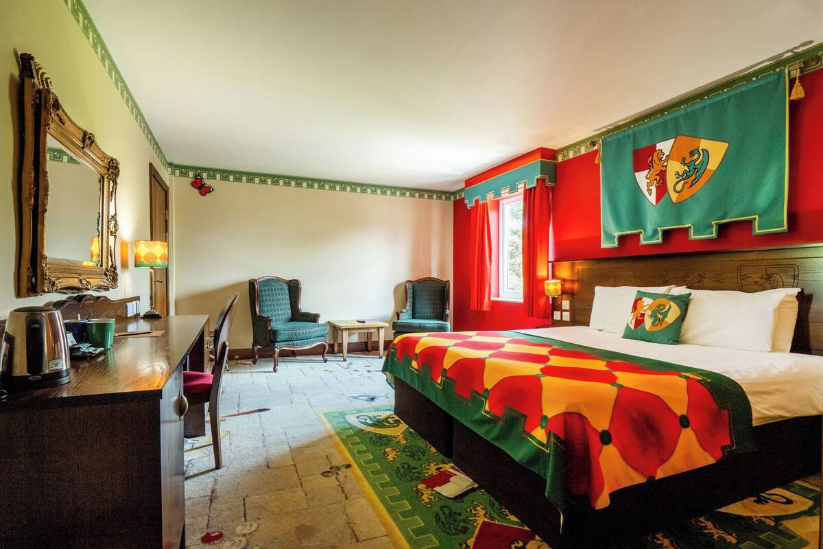 A hotel room with a bed, a desk, a chair, a mirror, and a window with curtains.