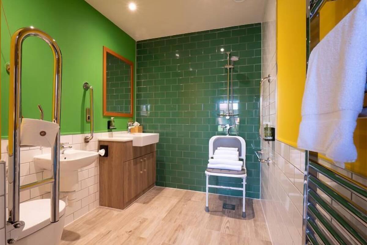 A bathroom with green walls, a wooden vanity, a white sink, a toilet, and a shower area.