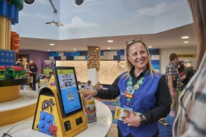 A woman in a blue vest with a badge, standing at a counter with a display of LEGO products. - Legoland Windsor Resort Hotel (Windsor)