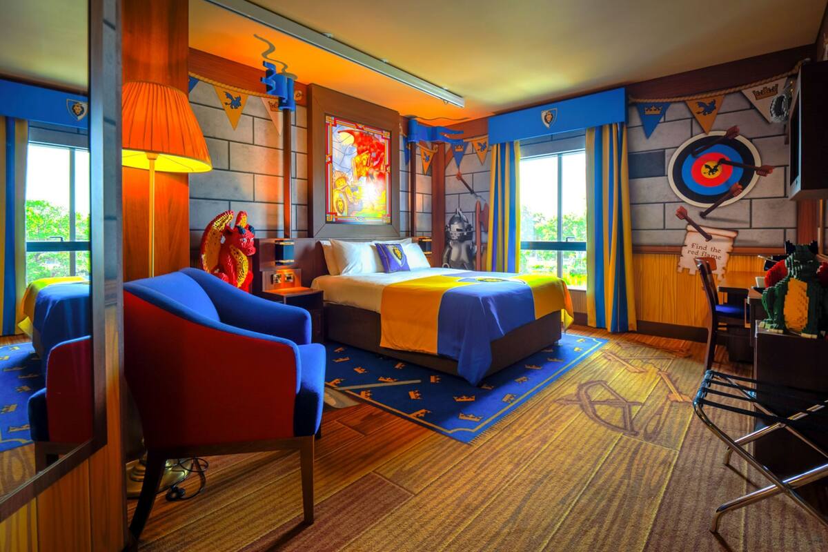 A hotel room with a large bed, a desk, and a chair. There is a window with a view of trees.