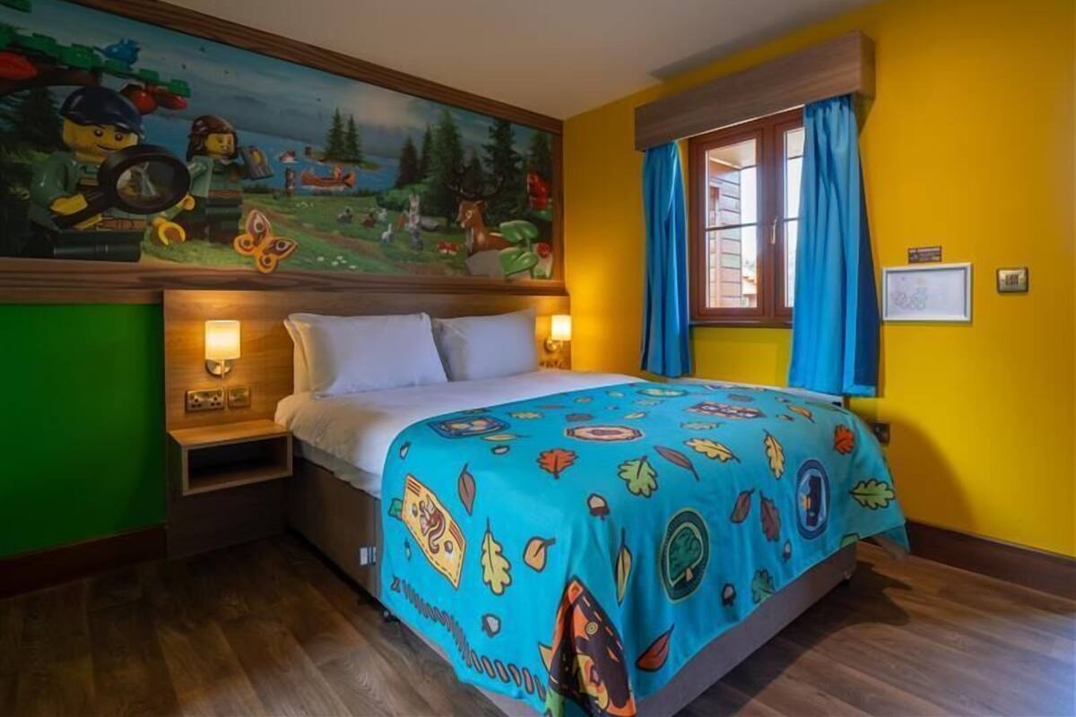 A hotel room with a bed, a mural on the wall, and a window with curtains.