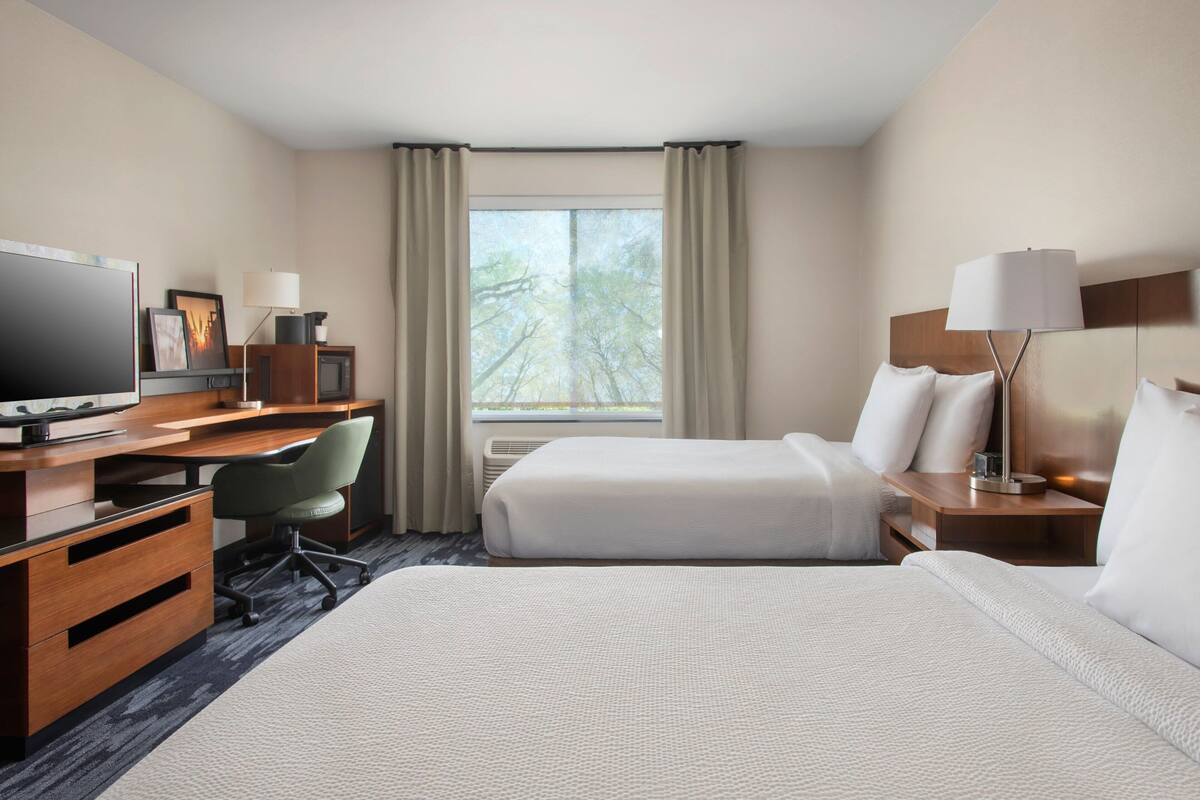 A hotel room with a bed, a desk with a computer, a chair, a TV, and a window with curtains.