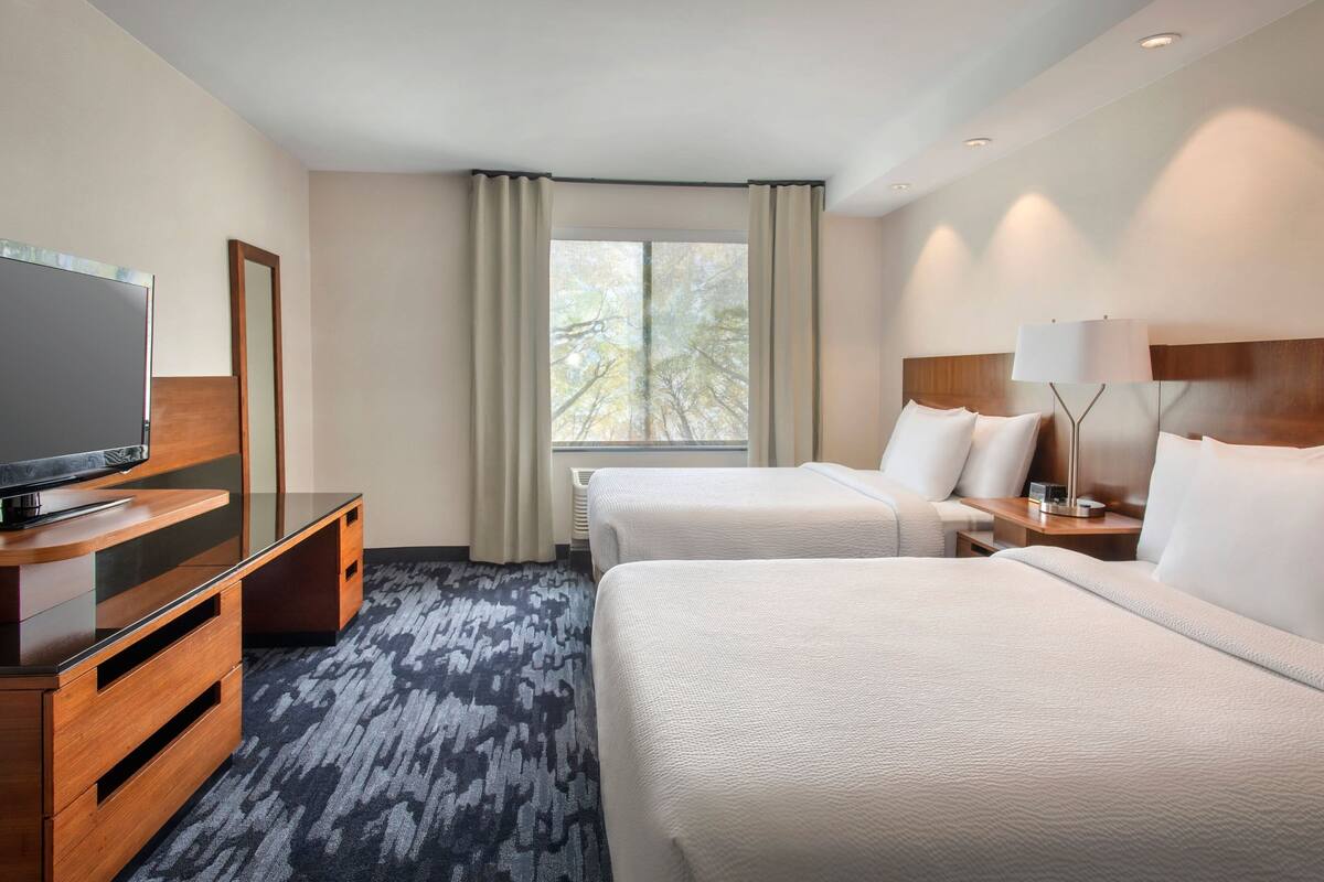 A hotel room with two beds, a TV, a dresser, and a window with curtains.