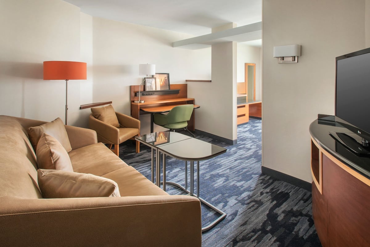 A modern hotel room with a sofa, a desk, a television, and a carpeted floor.