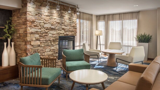 Un hall d’hôtel avec un mur en pierre, des fauteuils à revêtement vert, une table ronde blanche et un canapé beige.