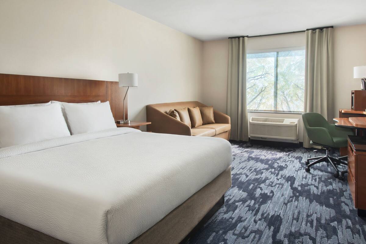 A hotel room with a large bed, a sofa, a desk, and a chair.