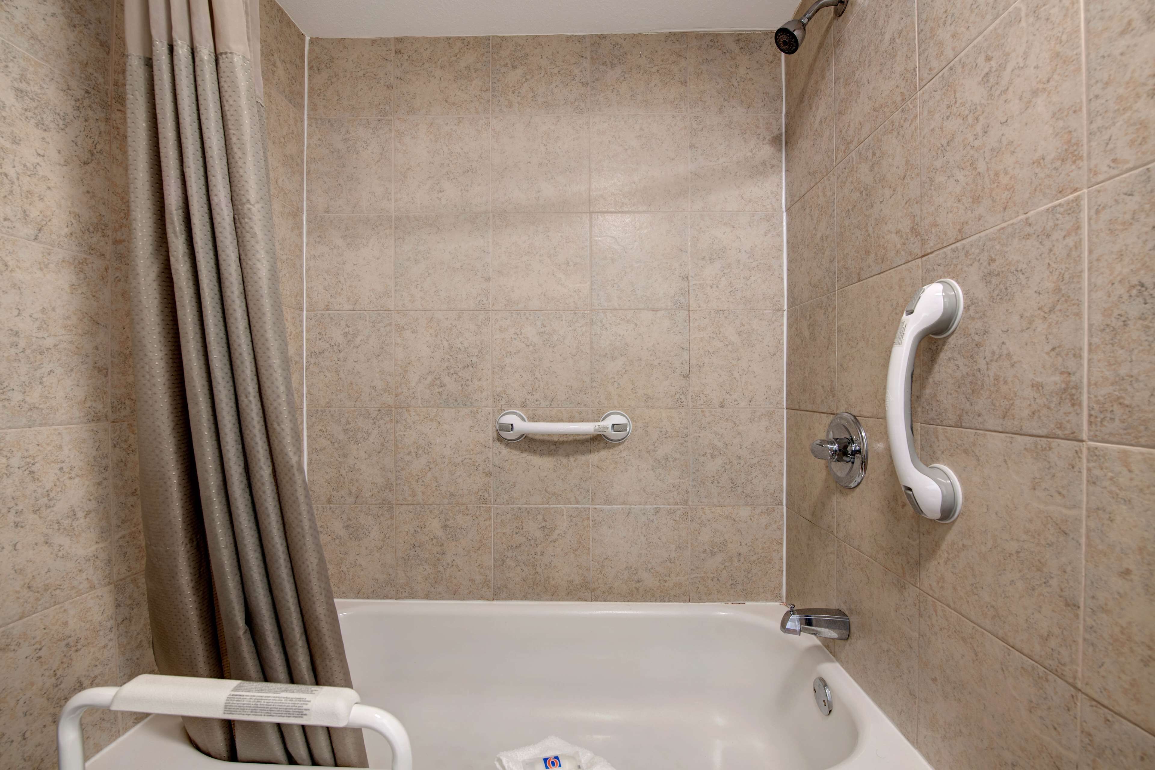 Un baño con bañera, barras de apoyo y cortina de ducha.