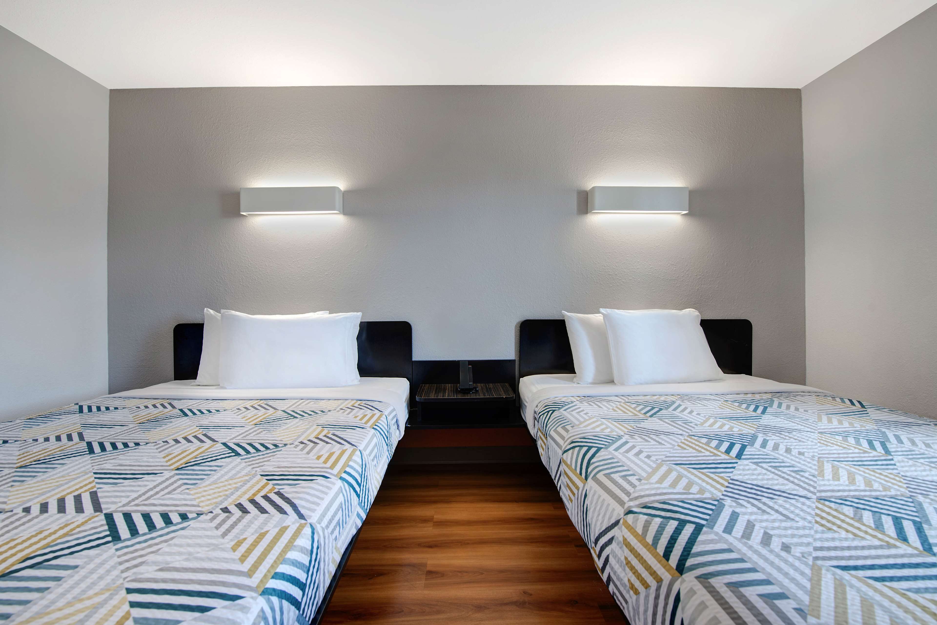A hotel room with two single beds, a wooden floor, and a nightstand between them.