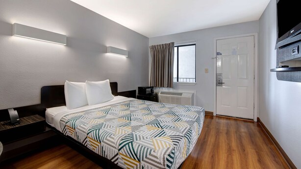 Una habitación de hotel con cama, escritorio, televisión de pantalla plana, ventana con cortinas y una puerta.