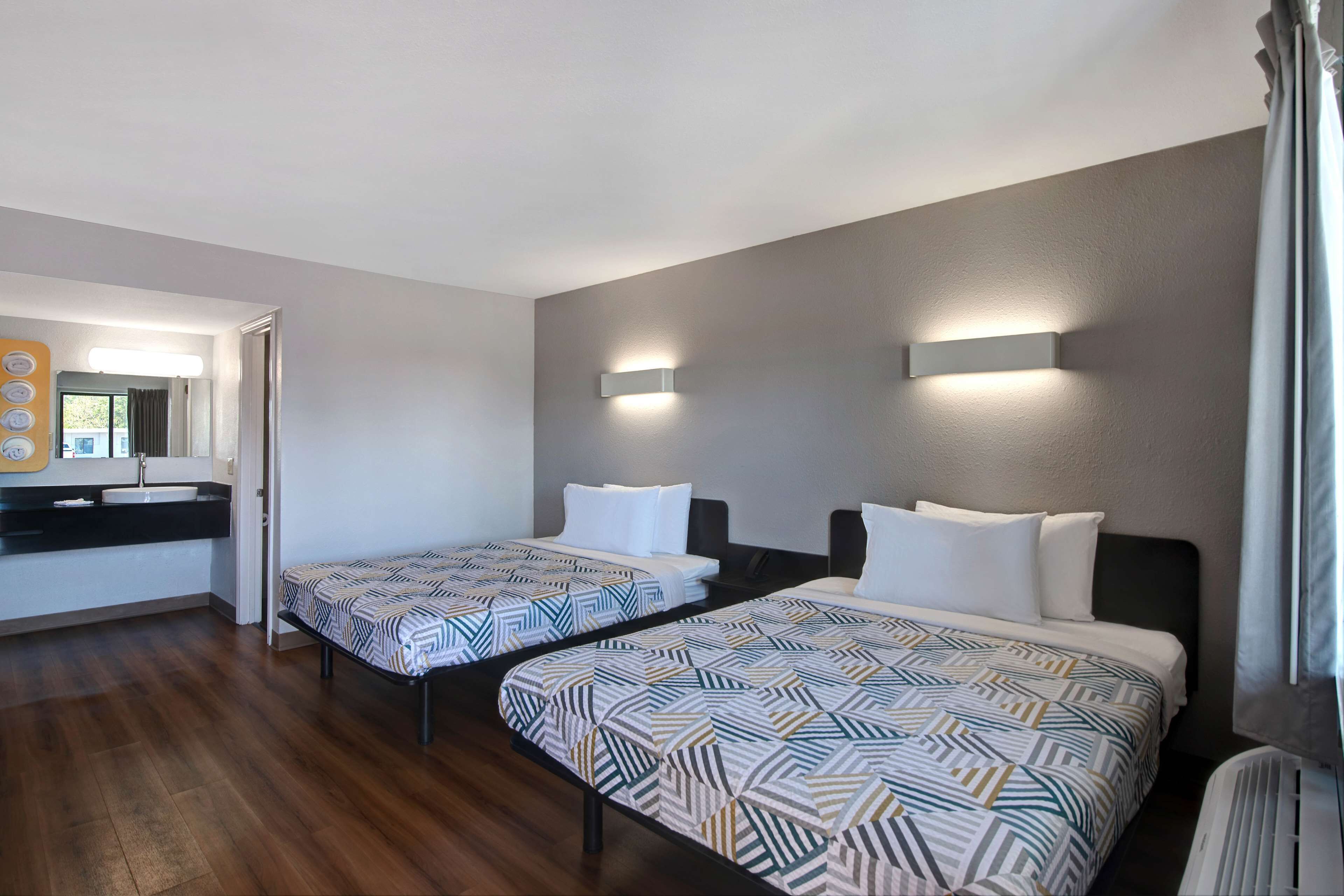 Habitación de hotel con dos camas, baño y una pequeña zona de estar.