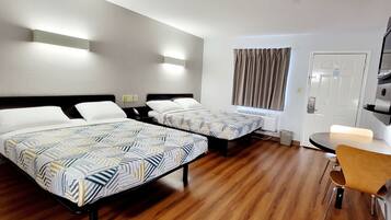 Una habitación de hotel con dos camas, una mesita, una silla y una ventana con cortinas.