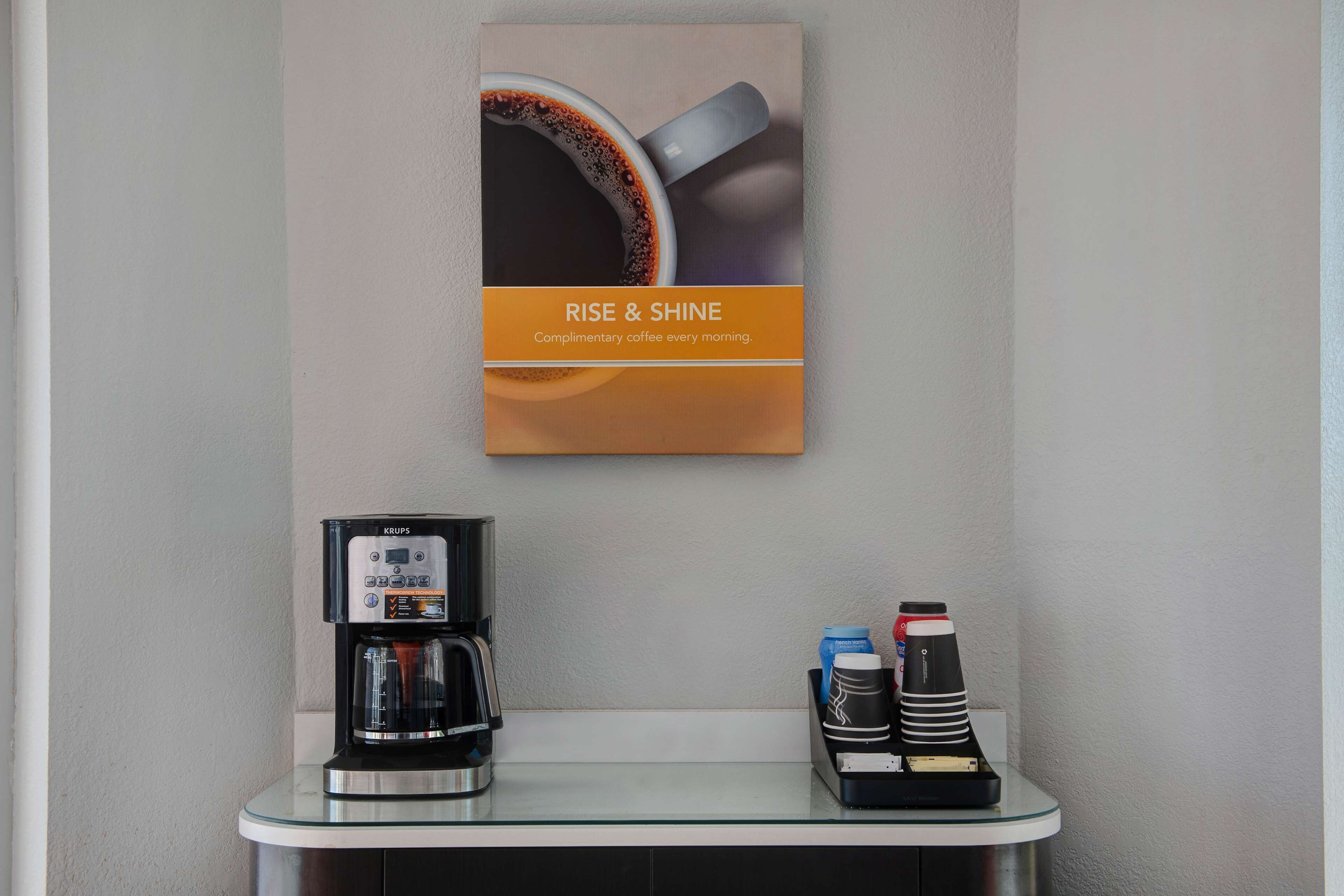 A coffee station with a Krups coffee maker, a coffee cup, and a coffee grinder on a glass counter.