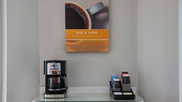 Una estación de café con una cafetera Krups, una taza de café y un molinillo de café sobre una encimera de vidrio.