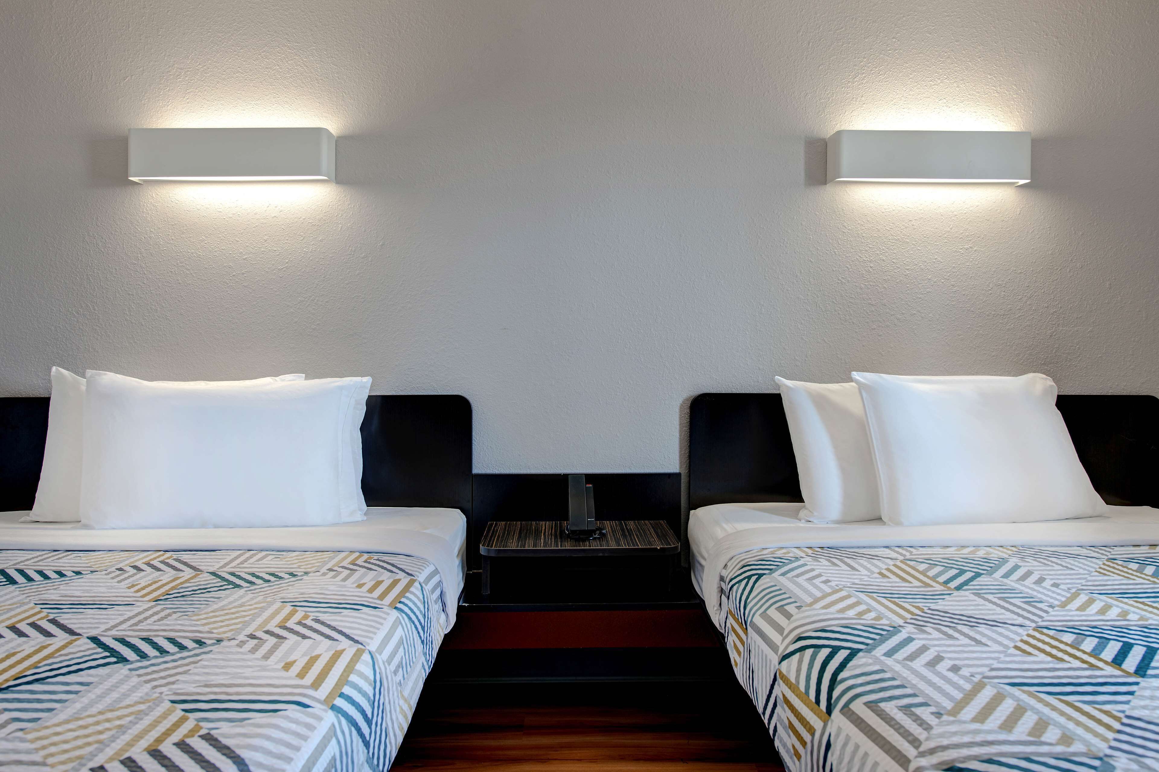 Habitación de hotel con dos camas, cada una con una colcha estampada, almohadas blancas y una mesita de noche entre ellas.