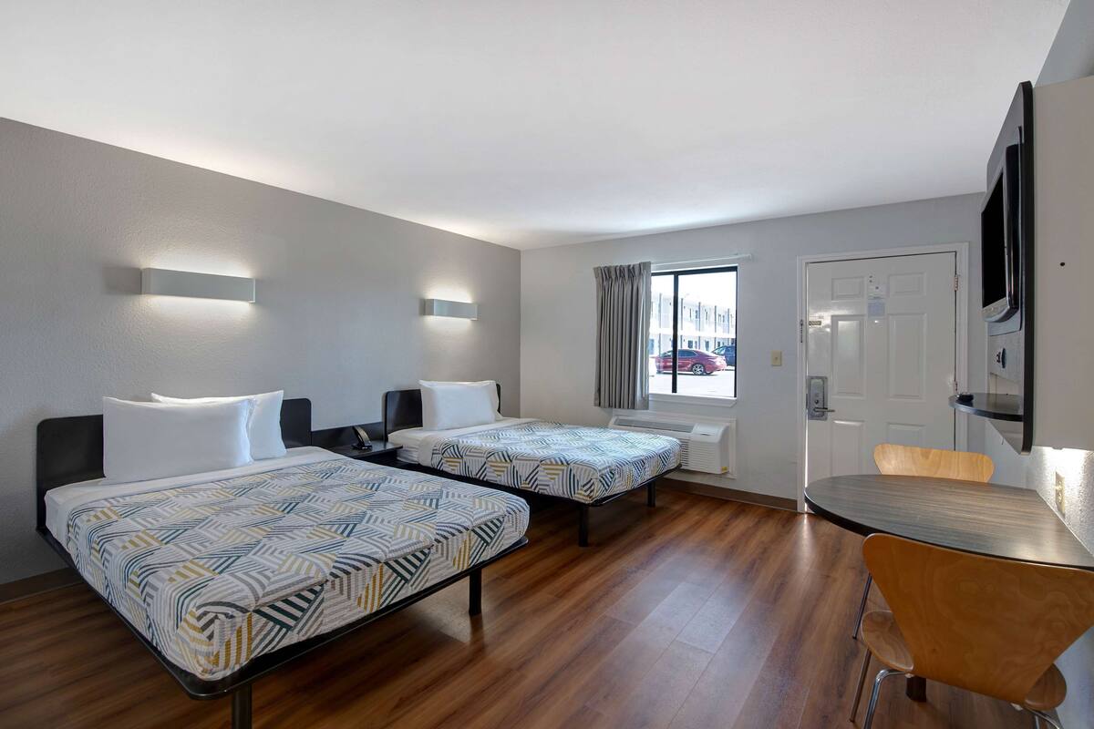 A hotel room with two beds, a small table, and a TV.