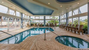 Una piscina interior con vistas despejadas al exterior, rodeada de sillones de descanso y un suelo de baldosas.
