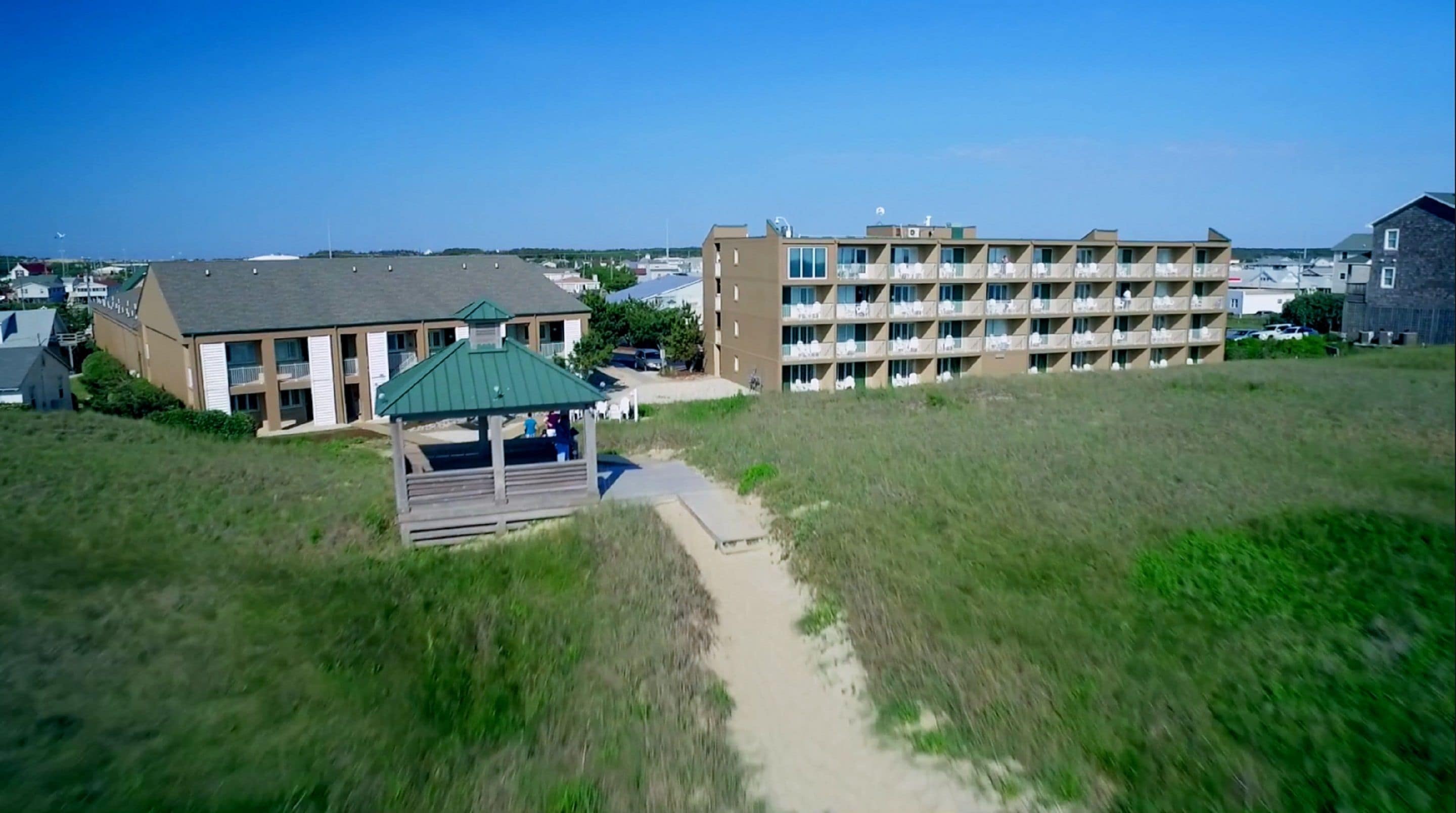 A multi-story hotel with a central courtyard, a covered seating area, and a beach view.