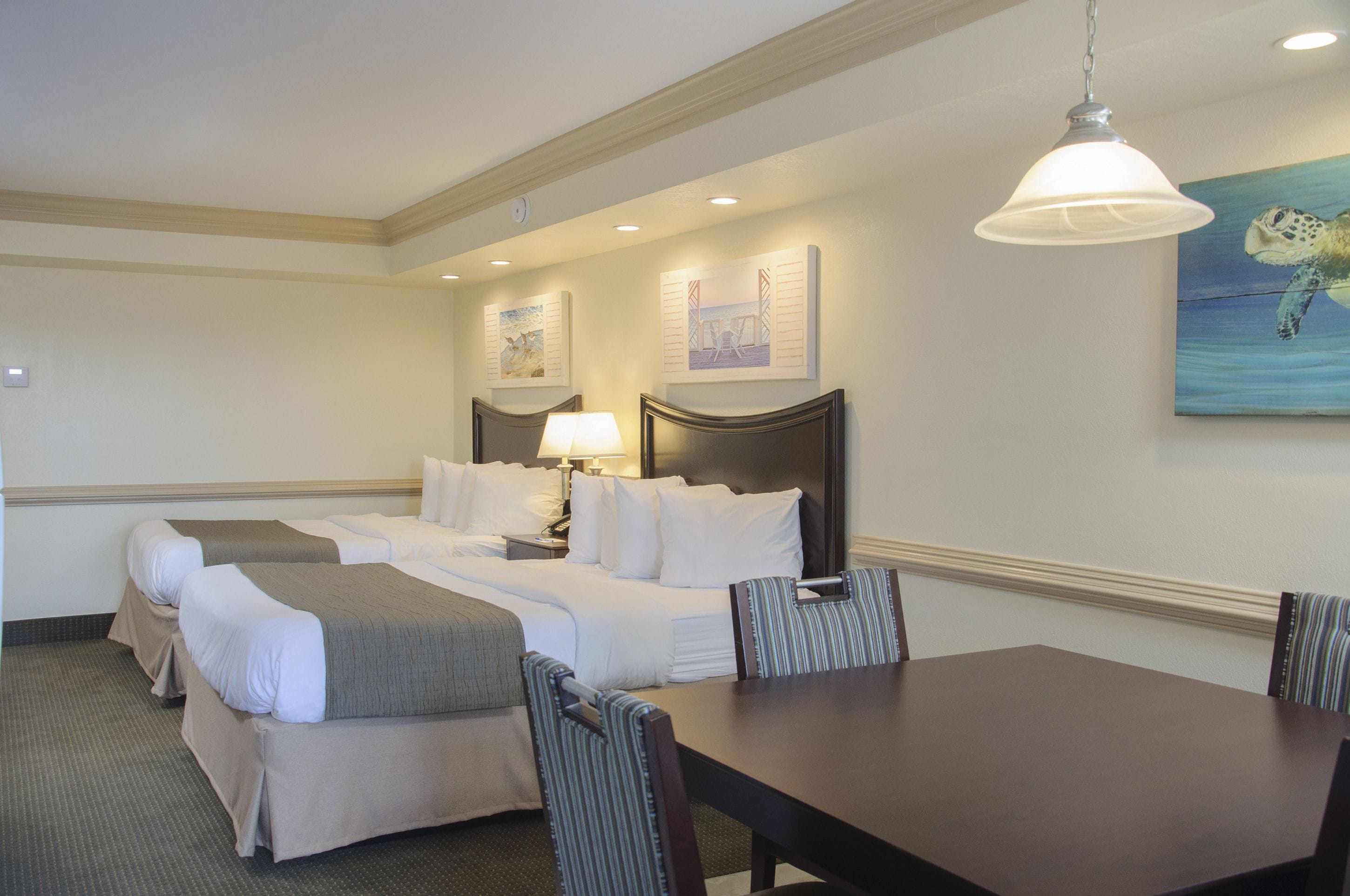 A hotel room with two beds, a dining table, and a painting of a sea turtle on the wall.