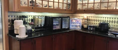 Een keuken met houten kastjes, een zwart aanrecht, een magnetron, een koffiezetapparaat en een koelkast.
