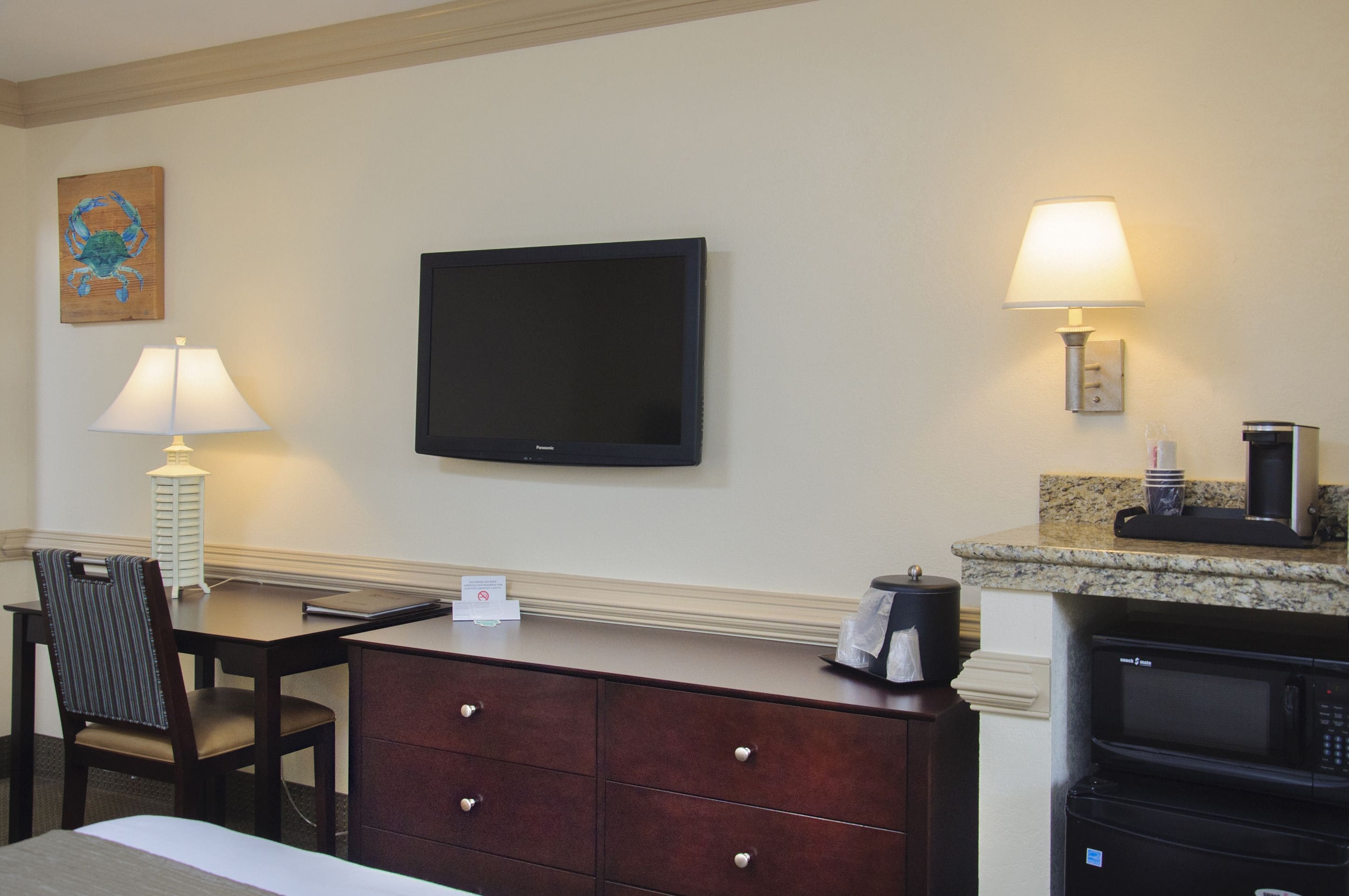 Hotelkamer met flatscreen televisie, bureau met lamp, stoel, dressoir, magnetron en koffiezetapparaat.