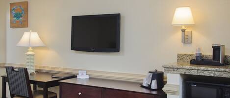 Habitación de hotel con televisión de pantalla plana, escritorio con lámpara, silla, cómoda, microondas y cafetera.