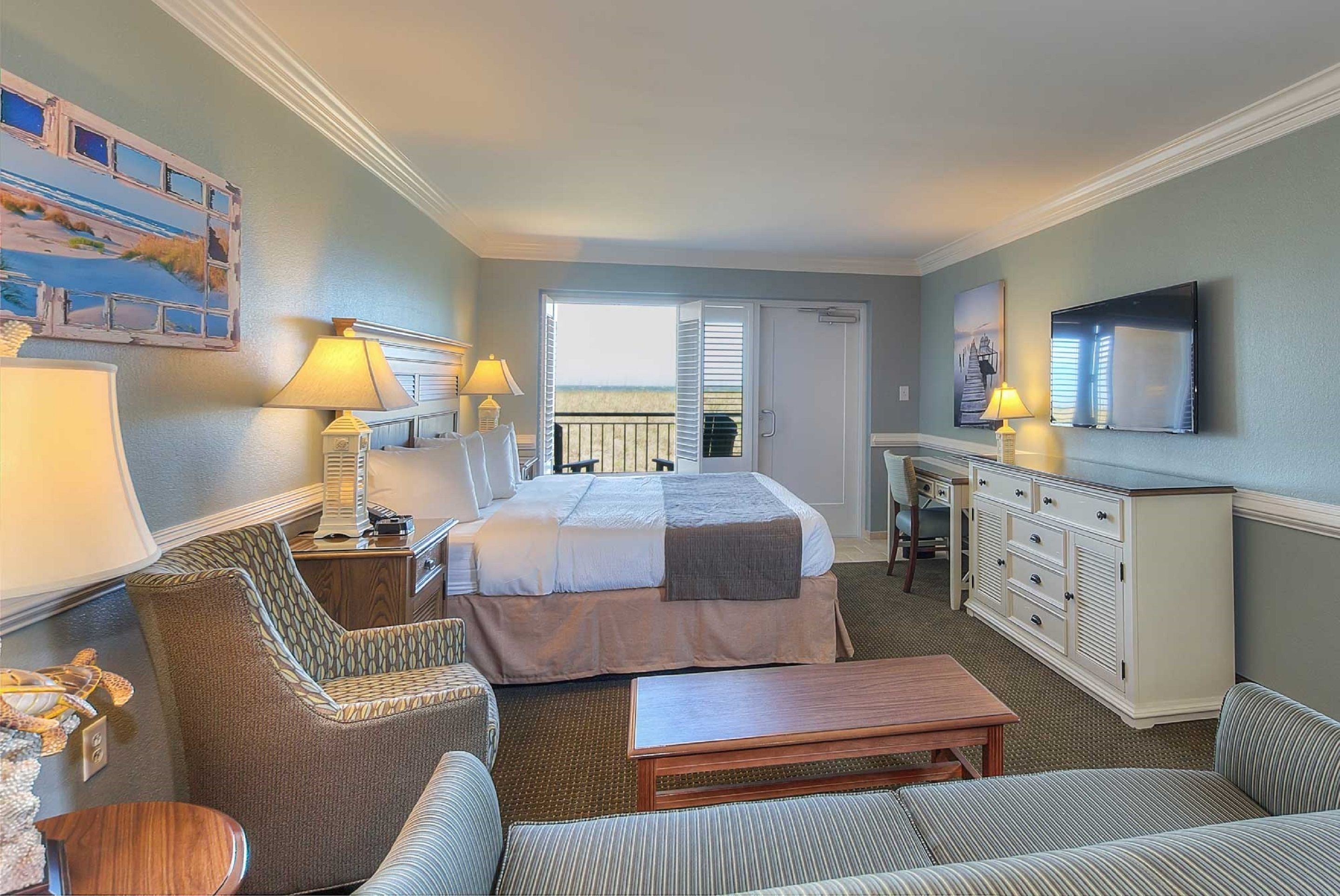 A hotel room with a bed, two chairs, a desk, a television, and a balcony with a view.