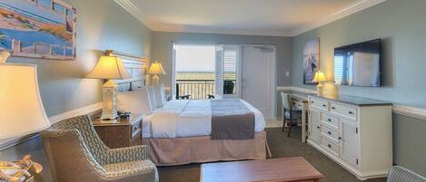 A hotel room with a bed, two chairs, a desk, a television, and a balcony with a view.