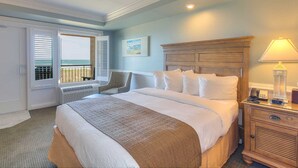 Habitación de hotel con una cama grande, una mesita de noche de madera, una silla, una ventana con persianas y vistas al exterior.